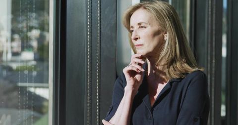 Thoughtful woman standing by office window in contemporary space