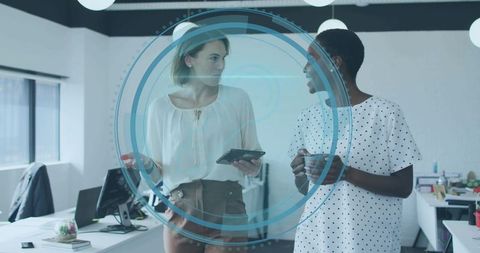Two Professional Women Collaborating with Tablet and Coffee in Modern Office with Digital HUD