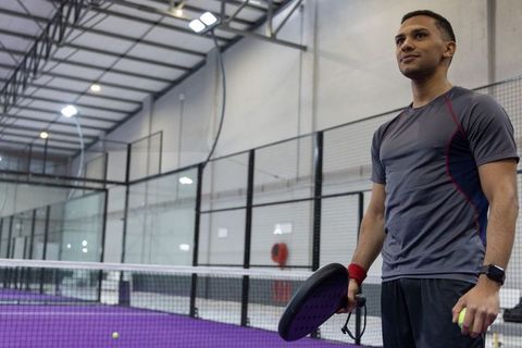 Athletic man holding padel racket and ball standing at indoor court with purple surface