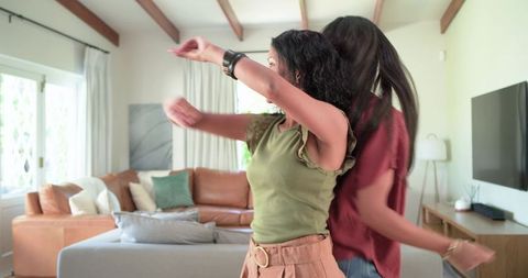 Joyful young women dancing and spinning in bright contemporary living room with sofa