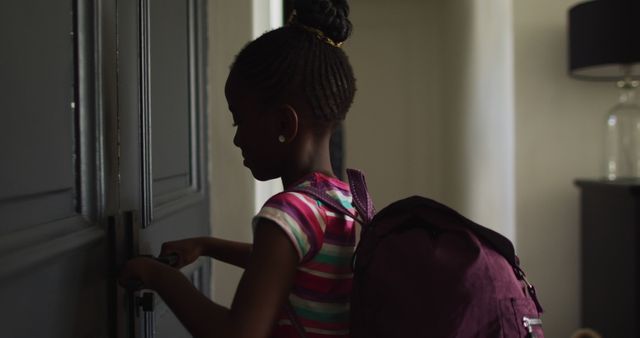 Image of african american girl with schoolbag opening front door and leaving home for school. Childhood and domestic life.