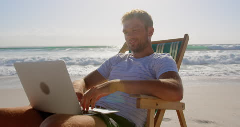 Man Relaxing on Beach Working on Laptop in Sunlight