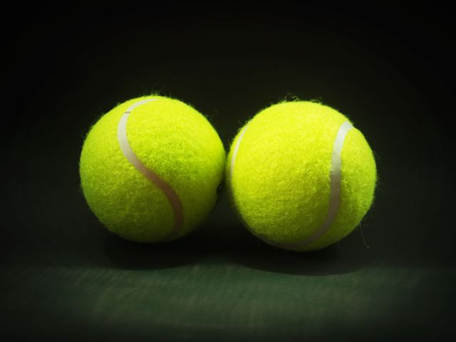 Two bright yellow tennis balls are centered against a dark background. Useful for sports-themed designs, promoting tennis events, or illustrating sports equipments. Ideal for advertisements, posters, web design, and educational material.