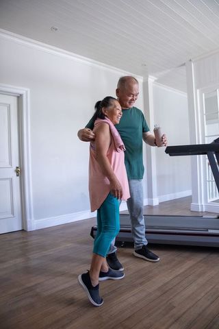 Senior couple working out together at home gym by treadmill, smiling and hydrating