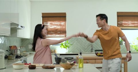 Happy couple cooking together in bright modern kitchen, dancing while preparing meal