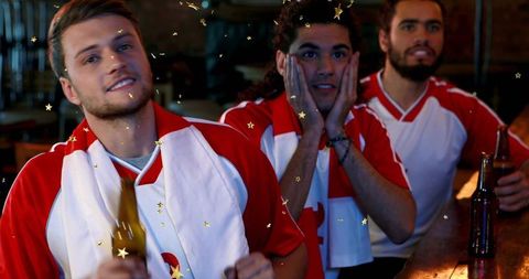 Young male fans cheering at sports bar holding beer celebrating with gold confetti