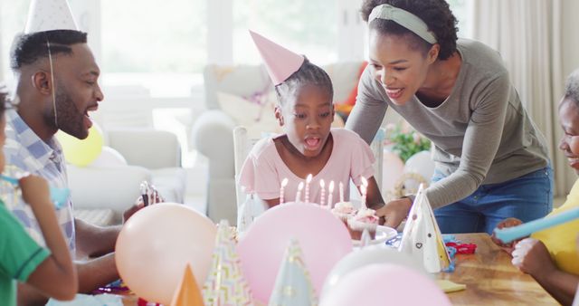 Happy african american family celebrating, daughter blowing out birthday cake candles, slow motion. Family, celebration and togetherness concept.