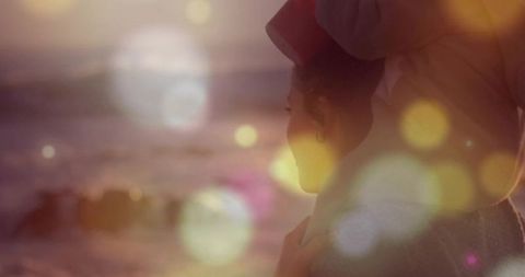Woman with turban overlooking sunset sea with bokeh effects