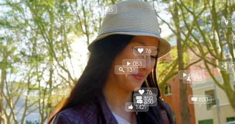 Young woman walking sunlit street in bucket hat and leather jacket with social ar icons