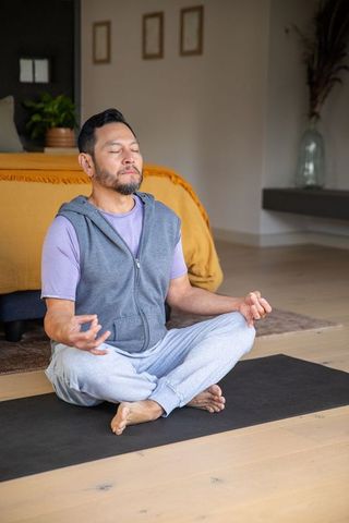 Mature asian man meditating on yoga mat in bedroom practicing mindfulness and serenity
