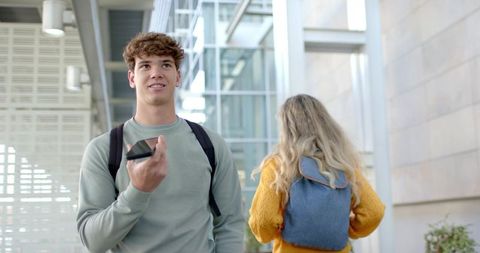 Male Student Speaking into Smartphone While Walking Through Modern Campus Atrium