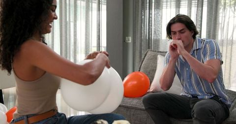Couple Blowing Up Balloons Preparations for Birthday Celebration