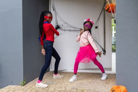 African american girls posing in playful halloween costumes on porch with spiderwebs