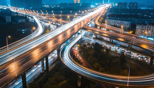 Night multilevel highway interchange with flowing light trails on reflective roads