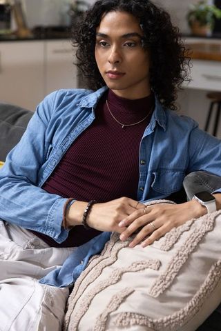 Nonbinary person relaxing on sofa checking smartwatch and tracking health metrics