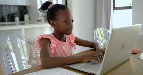 Young African Girl Studying on Laptop at Sunlit Kitchen Table for Remote Learning