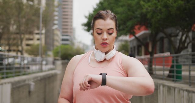 Happy plus size caucasian woman fitness training in city looking at smart watch. City living, fitness and modern urban lifestyle.