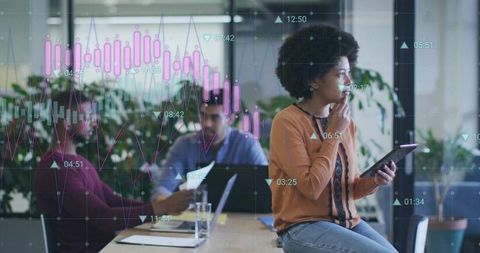 Young professional woman analyzing interactive data on tablet while team collaborating in office