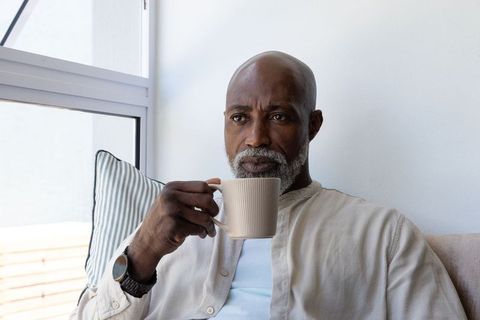 Contemplative senior african man sipping coffee on sofa by window for relaxed lifestyle