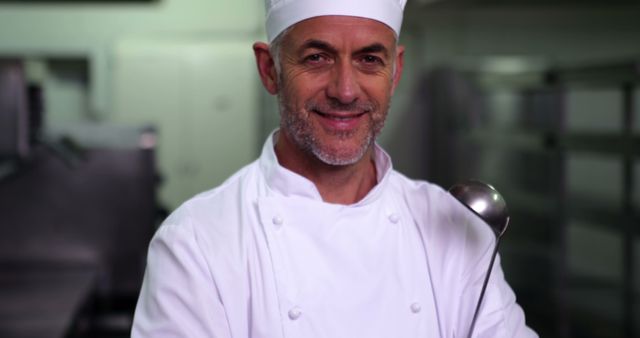 Experienced chef standing in an industrial kitchen, holding a spoon. Chef is dressed in traditional white uniform and hat, smiling with confidence. Ideal for use in culinary blogs, restaurant promotions, cooking classes, or educational materials showcasing professional culinary experience.