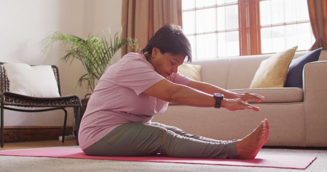 Senior woman performing stretching exercises on a yoga mat in a living room. Well-suited for content related to home workouts, senior fitness, self-care routines, and healthy lifestyles. Ideal for promoting fitness programs for seniors, indoor exercise routines, and wellness practices.