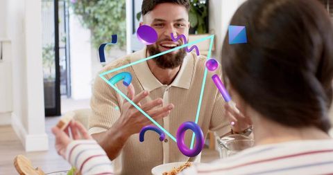 Bearded man smiling and gesturing at dining table with colorful augmented reality graphics