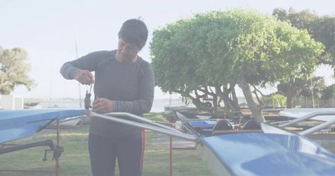 Female rower repairing rigging on blue rowing shell with wrench at marina maintenance