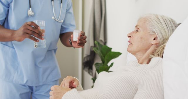 Image of midsection of african american male doctor giving water to caucasian senior woman. seniors health and nursing home lifestyle concept.