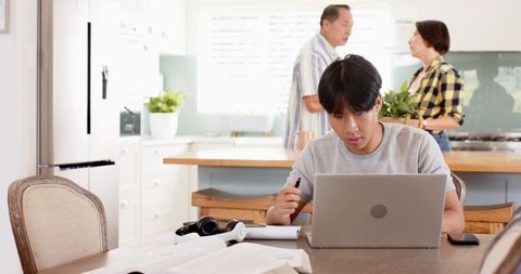 Serious Teen Studying in Family Kitchen with Laptop and Books