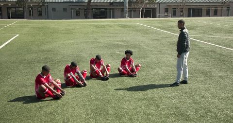 Coach instructing young soccer players stretching on field