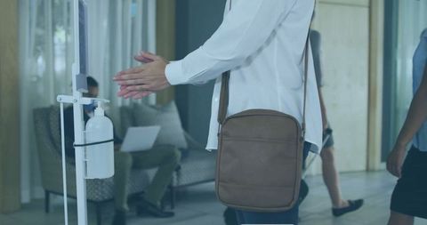 Woman applying hand sanitizer in modern lobby with crossbody bag