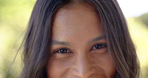 Smiling woman close-up portrait with long dark hair sunlit natural bokeh outdoors warm glow