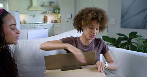 African american roommates unpacking moving box on couch in bright modern living room home
