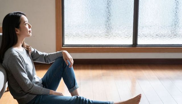 Calm asian woman sitting and gazing through frosted window in sunlit minimalist room
