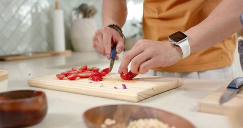 Asian man slicing cherry tomatoes on wooden cutting board wearing smartwatch