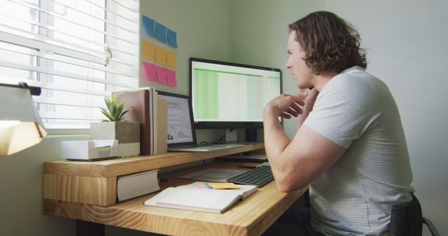 Young professional is working on a spreadsheet at a home office desk, displaying concentration and productivity. Ideal for illustrating concepts of remote work, modern job dynamics, technology use, and efficient home-based work environments.