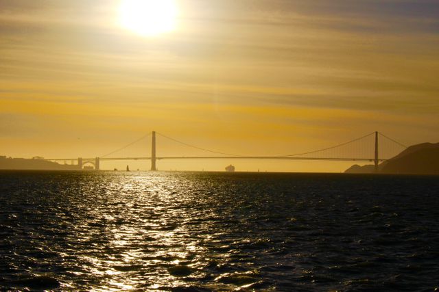 Golden Gate Bridge silhouetted against a glowing sunset with shimmering waters below. Ideal for travel blogs, tourism advertisements, website headers, or wall art. Perfect for content highlighting San Francisco or iconic architectural landmarks.
