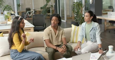 Diverse team collaborating and brainstorming on sofa with laptop in modern open-plan office