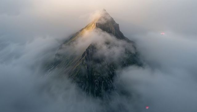 Sharp alpine peak piercing low clouds at dawn, warm summit light and misty ridge