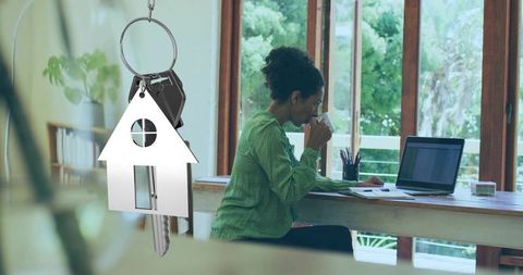 Sipping coffee while reviewing laptop in bright home office with house keychain