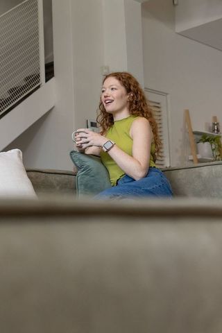 Redhead woman relaxing on sofa holding mug, modern minimalist living room lifestyle