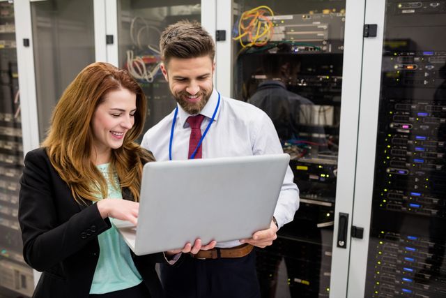 Two IT professionals are collaborating in a server room, using a laptop to analyze server data. This image is ideal for illustrating teamwork in technology, IT support services, data management, and modern business environments.