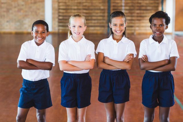 This image shows a diverse group of school kids standing with their arms crossed in a gym, wearing uniforms. Ideal for educational materials, school brochures, advertisements for physical education programs, and articles on childhood development and teamwork.
