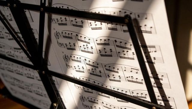 Sunlight casting grid shadows over classical piano sheet music on black metal stand