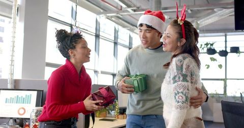 Diverse coworkers exchanging gifts and celebrating Christmas party in open-plan office