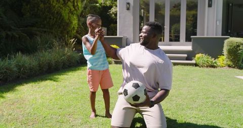 Father and Son Playing and Laughing with Soccer Ball in Front Yard