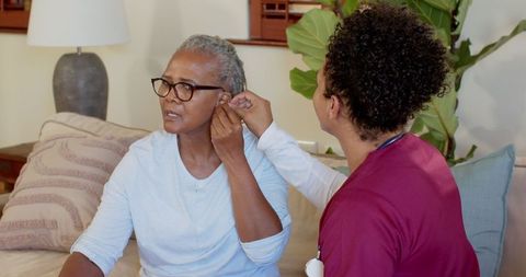 Senior woman assisted by male nurse adjusting hearing aid at home