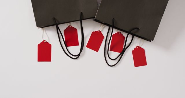 Black shopping bags with red sale tags hanging from them on white background create a striking visual. This image is ideal for promoting retail sales, discounts, and special shopping events. It can be used in advertising campaigns, social media posts, online stores, blog articles about shopping and consumer behavior, and print marketing materials to attract customers and highlight sales events.