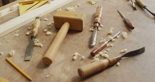 This image captures a close-up view of various woodworking tools on a workbench surrounded by wood shavings. It includes a wooden hammer, chisels, and a pencil, reflecting a traditional carpentry setting. This visual can be used to represent craftsmanship, DIY projects, woodworking tutorials, and artisanal skills in promotional materials, educational content, or blogs.