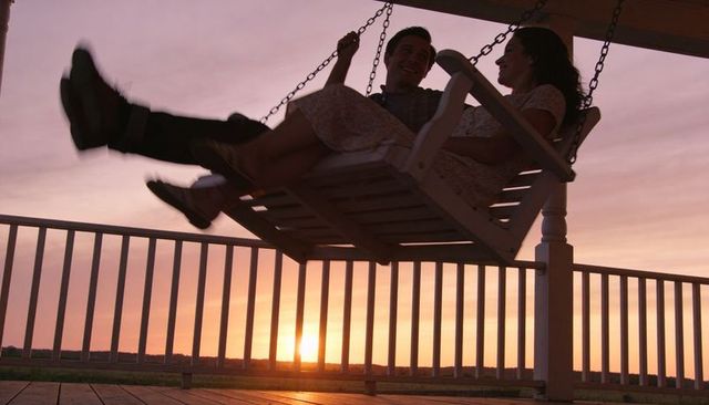 Couple swinging on porch swing at sunset silhouette on wooden deck
